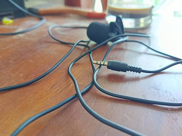 istock lavalier microphone resting on a wooden surface, accompanied by a slightly tangled cable. The scene is enriched with a paintbrush and a glass mug containing coffee, creating an atmosphere that blends multimedia production with creativity 2217910503