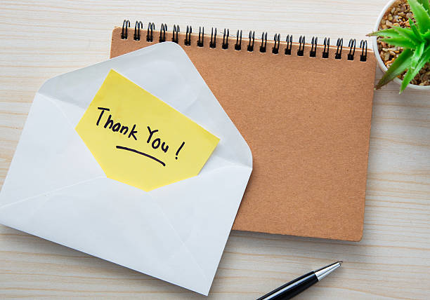 istock Thank you note emerging from envelope near notepad and pen on wooden desk 2217920513