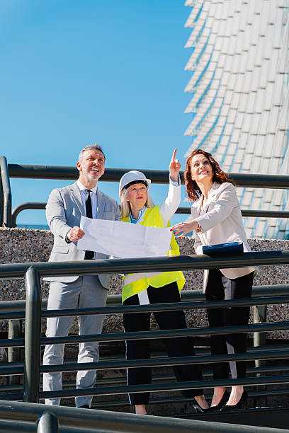 istock Professional architects reviewing blueprint, gesturing at modern building exterior, collaborating on architectural design project 2217927486