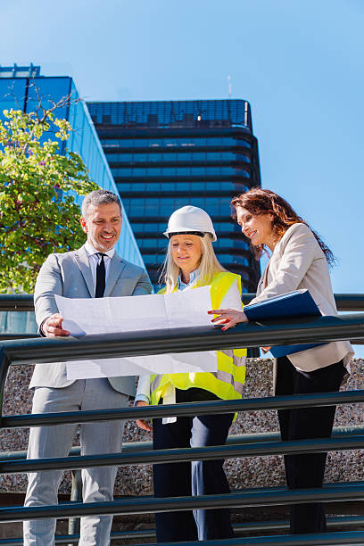 istock Professional architects collaborating near modern building, reviewing construction blueprints and sharing design insights during project planning meeting 2217927492