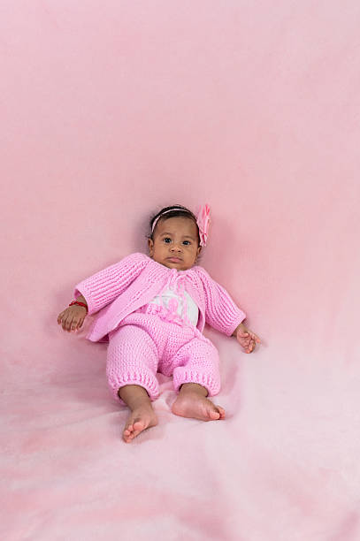 Cute baby girl relaxing on a pink blanket, wearing a pink knitted outfit and headband, creating a sweet and innocent scene