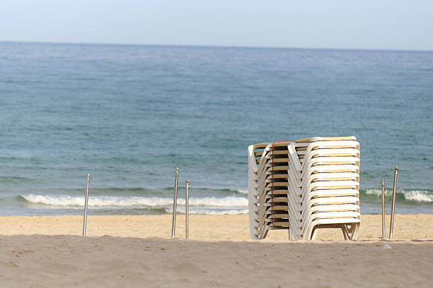 Stacked beach chairs on a tranquil sandy shore with gentle ocean waves.