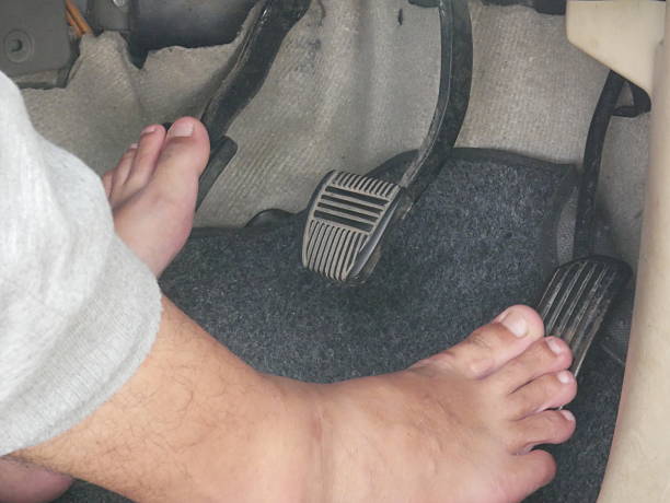 An unshod foot pressing down on the car’s pedal.