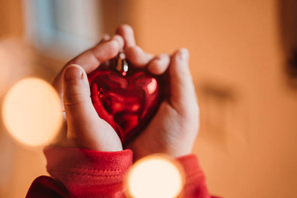 Hands Holding Red Heart Ornament with Warm Glow