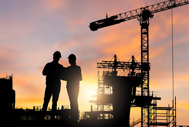 istock Silhouette of Engineers Against a Sunset Sky, Two Construction Workers Overseeing Project at Dusk, Engineers and Crane Silhouette at Sunset Construction Site 2217939538