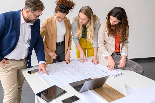 istock Business people examining blueprint and working on new project with computer and mobile phones on table in office 2217939723