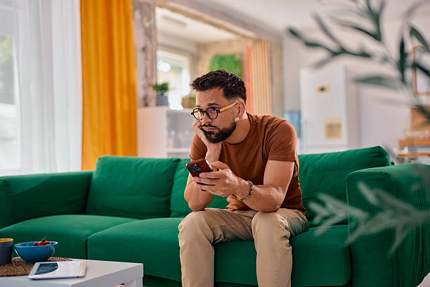 istock Bored man sitting on sofa looking at smartphone at home 2217946330