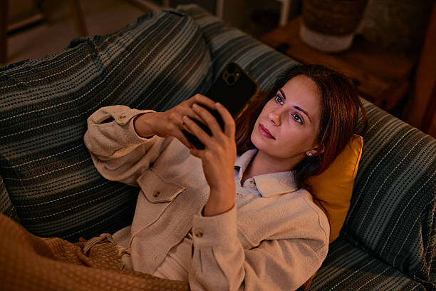 istock Woman relaxing on sofa using mobile phone in warm evening light 2217946352