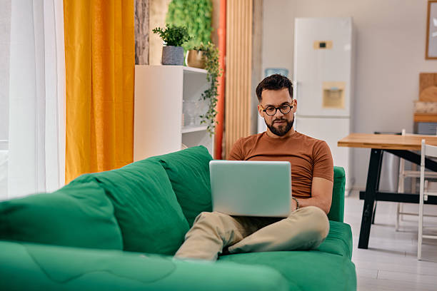 istock Young man working from home sitting on a green sofa using a laptop 2217946375