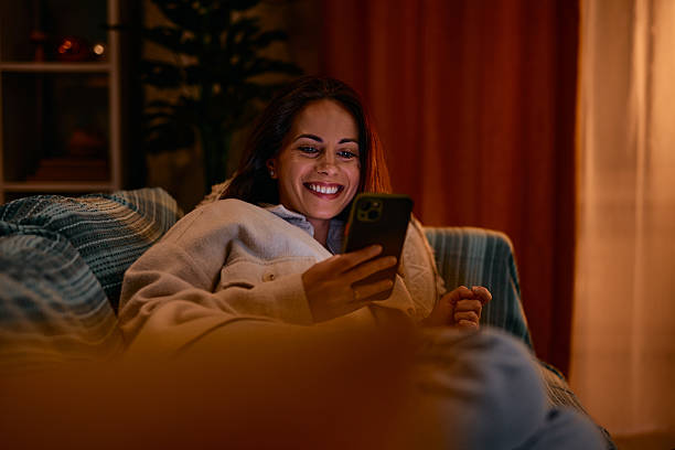 istock Young woman is using mobile phone and smiling while relaxing on sofa at home 2217946397