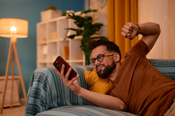 istock Bored man stretching and looking at smartphone while lying on sofa 2217946450