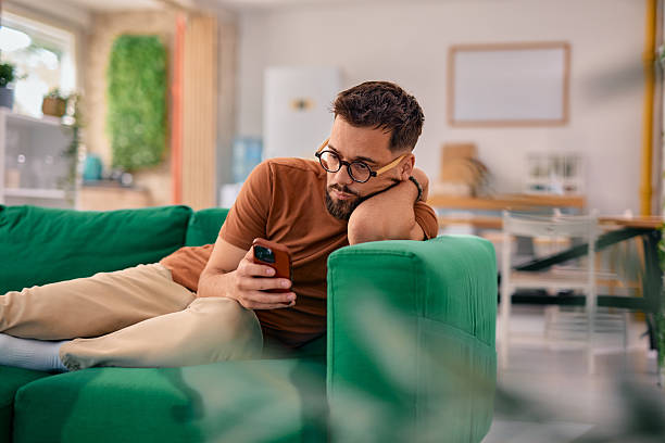 istock Bored young man lying on the sofa using his smartphone 2217946541