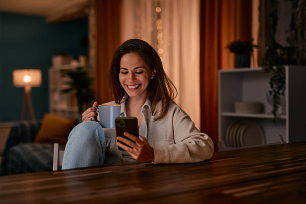 istock Smiling woman using smartphone and drinking coffee at home 2217946591