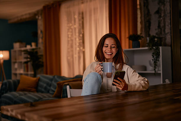 Young woman is enjoying a cup of coffee while using her phone at home
