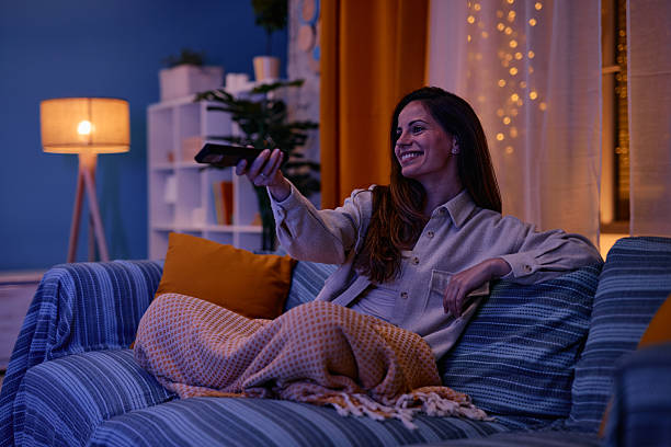 istock Young woman relaxing on sofa watching television changing channels with remote control 2217946633