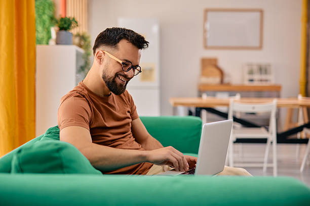 istock Smiling young man working from home sitting on a green sofa using a laptop 2217946641