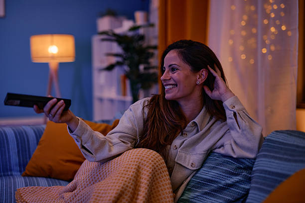 istock Woman relaxing on sofa watching television changing channels with remote control 2217946667