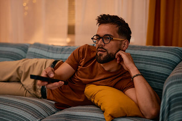 istock Young man lying on the sofa watching television, holding remote control 2217946714