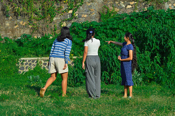 As the girls stand in a field, one raises her hand to point out something interesting nearby.
