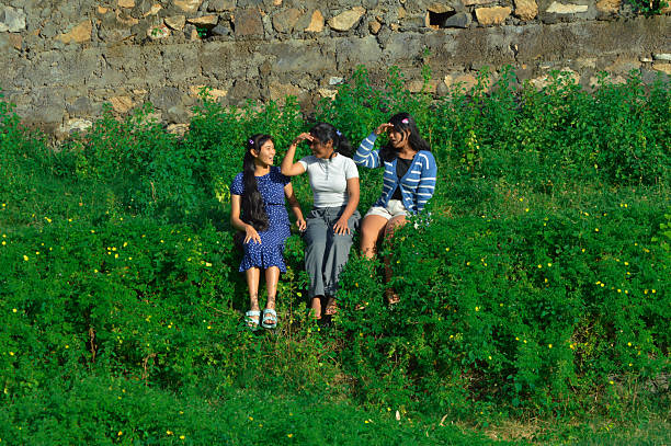 Two of the girls raise their hands to block the sunlight as they chat and laugh on the overgrown terrace.