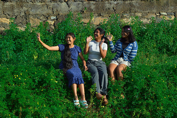 Sitting together in the sunshine, one girl waves with excitement while the others enjoy the moment.