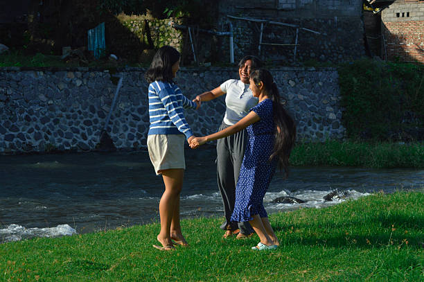 Enjoying the moment, the girls laugh and spin hand-in-hand in the lush green field near the river.