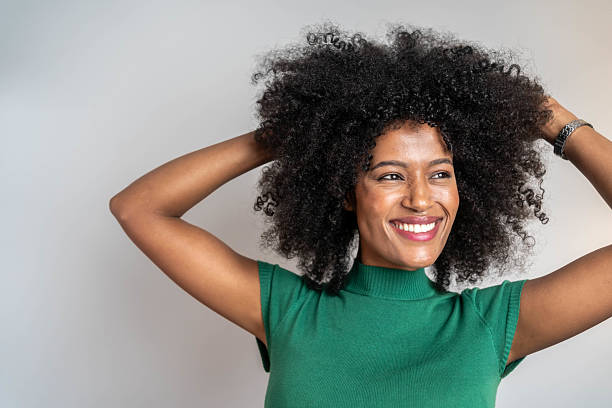 Beautiful African American girl with afro hairstyle smiling, looking at camera, cheerful expression, isolated on grey background, studio shot.