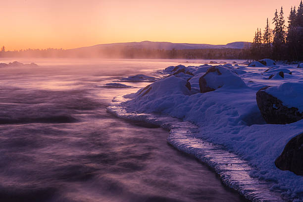 River ice reflects vibrant sunset hues during a winter evening in Norway