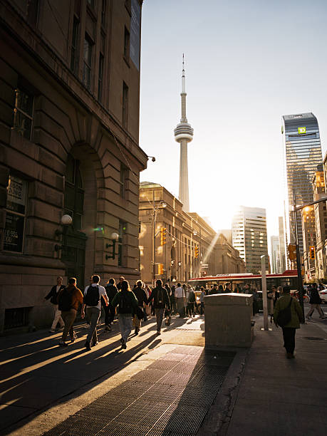 Toronto, Ontario, Canada – October 2014: Commuters walk along Front Street during sunset in downtown Toronto, with the CN Tower and Union Station in the background, casting long shadows in the golden light.