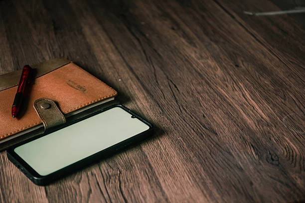 A book, a smartphone with a white screen, and a white glass are on the table.
