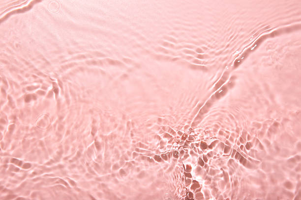 Rippled surface of clear water on pink background, top view