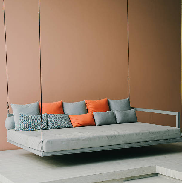 Sofa concept. Modern minimalist swing sofa design with colorful cushions in contemporary indoor setting against brown wall