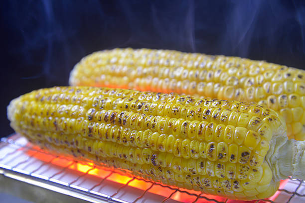 Grilling corn on a charcoal grill with rising smoke