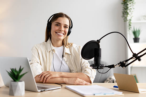 istock Happy female podcaster recording audio content using laptop and microphone looking at camera 2217995916
