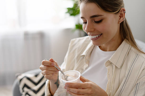 istock Smiling woman enjoying yogurt on comfortable sofa at home 2217995931