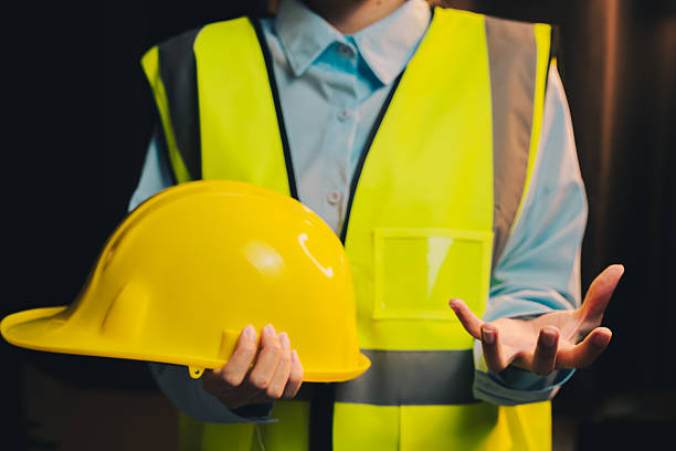 istock Engineer concept. Construction Worker in Safety Vest Holding Yellow Hard Hat with Outstretched Hand Presenting Information 2217999516