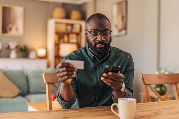 istock Focused man making online payment using smartphone and credit card at home 2218000446