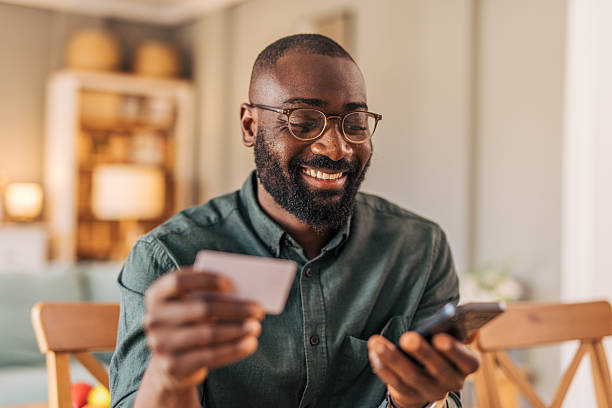 istock Smiling man making online payment using credit card and smartphone at home 2218000466