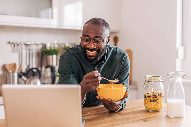 istock Smiling man eating breakfast and watching laptop in kitchen 2218001450