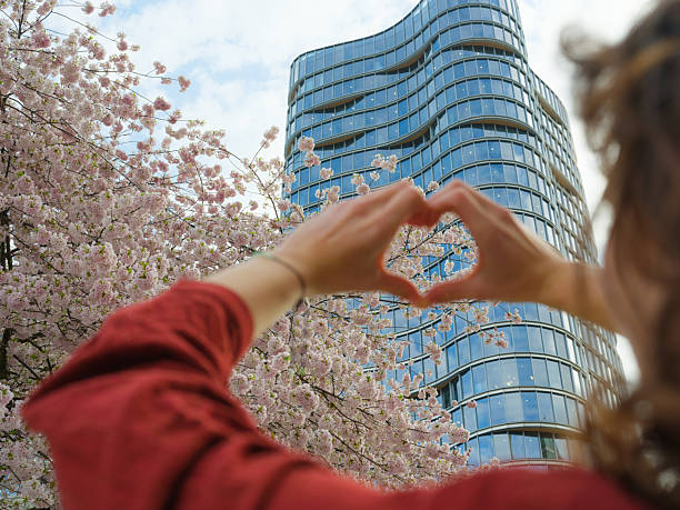 Woman showing heart  gesture on the background of cherry blossoms  in springtime