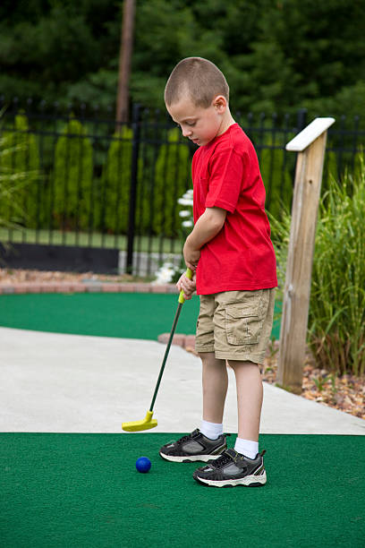 istock Young boy concentrating on putting ball in mini golf 2218006628