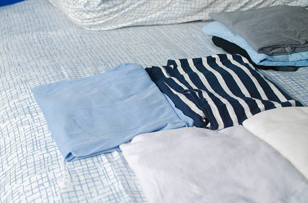 A top-down view of folded casual clothes arranged on a neatly made bed with a light patterned bed sheet. Minimalist home lifestyle and organization concept.