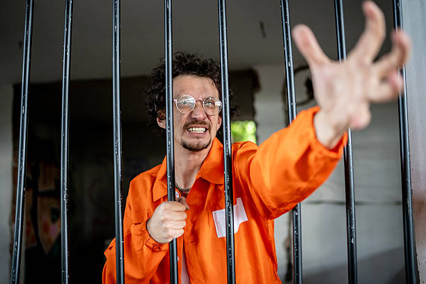 istock Man Grasping Behind Bars in an Orange Prison Uniform 2218009752