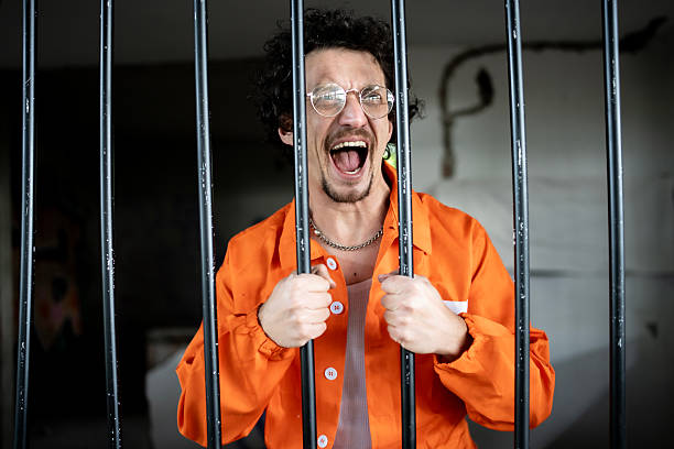 istock Frustrated Man in Jail Cell Wearing Orange Prison Jumpsuit 2218009753