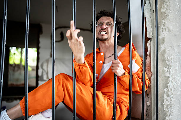 istock Prisoner in Orange Uniform Expressing Defiance Behind Jail Bars 2218009758