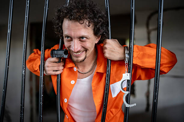 istock Inmate Holding Gun Behind Bars in an Orange Prison Jumpsuit 2218009762