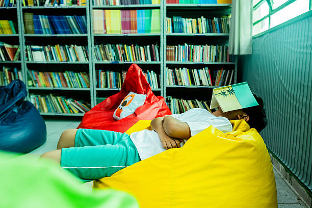 istock Schoolboy napping with a book on his face in a school library 2218009863