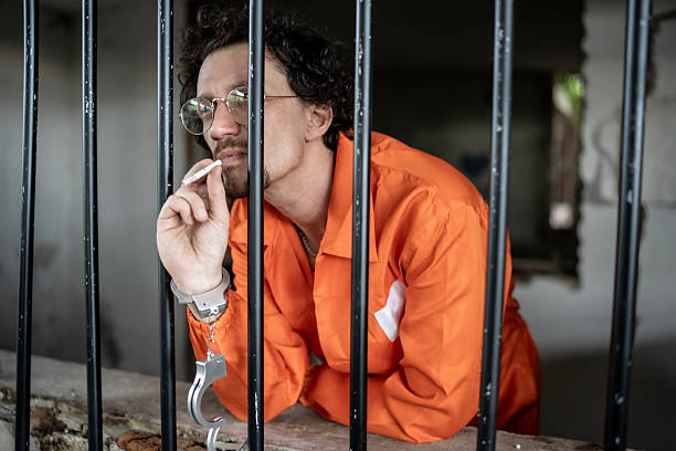 istock Man in Orange Uniform Leaning on Prison Bars in Deep Thought 2218009866