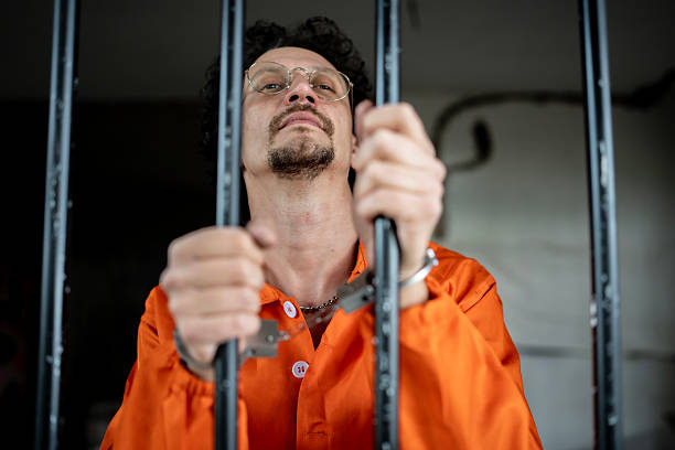 istock Man in Handcuffs Behind Jail Bars in Orange Prison Uniform 2218010052