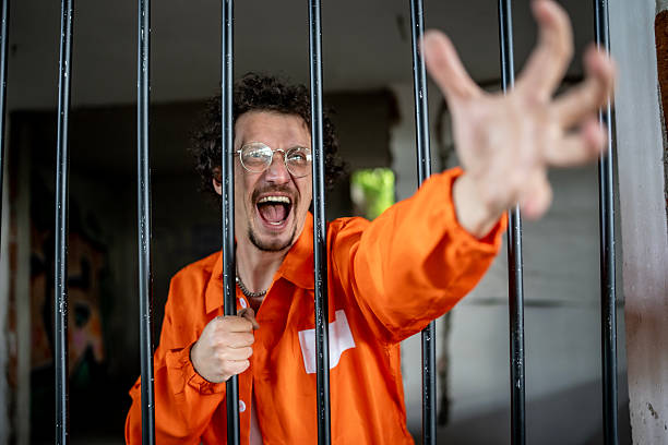 istock Excited Man Behind Bars Reaching Out in Orange Prison Uniform 2218010087